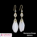 A pair of gold-tone drop earrings with clear rhinestone accents and large, teardrop-shaped milky white beads, labeled 'Romance Drops E819-6' on a black background with a Legacy Jewelry & Accessories logo.
